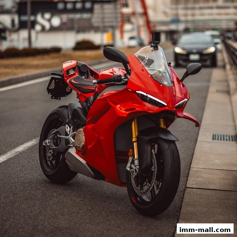 A vibrant red sports motorcycle parked on the side of a road with a car in the background.