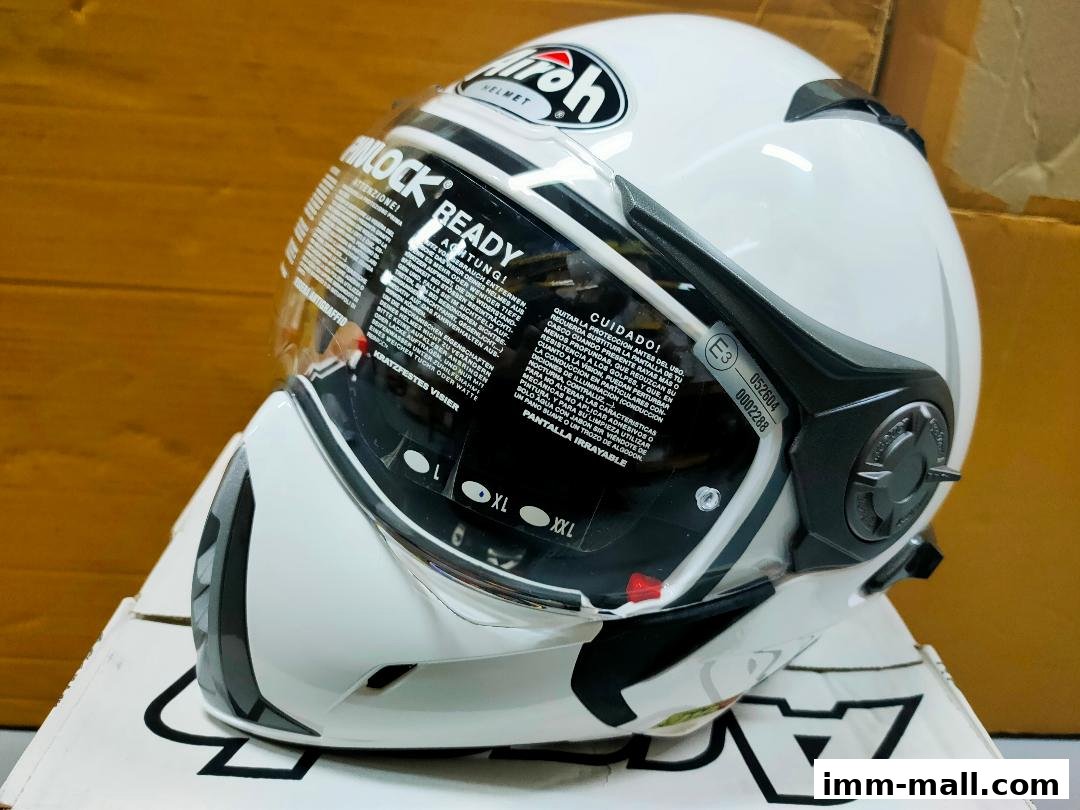 A white Airoh motorcycle helmet with a clear visor and multilingual warning labels.