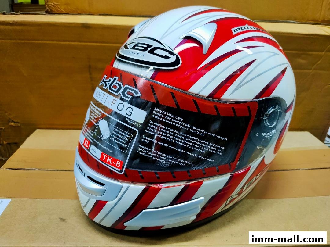 A close-up of a white and red KBC motorcycle helmet with an anti-fog visor.