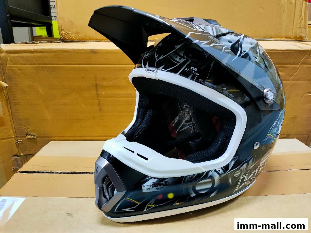 A black and white motocross helmet with a graphic design, displayed on a cardboard box.