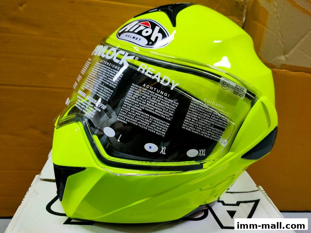 A bright yellow Airoh motorcycle helmet with a clear visor and various warning labels.