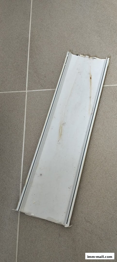 A white metal strip with some dirt and rust stains on a tiled floor.