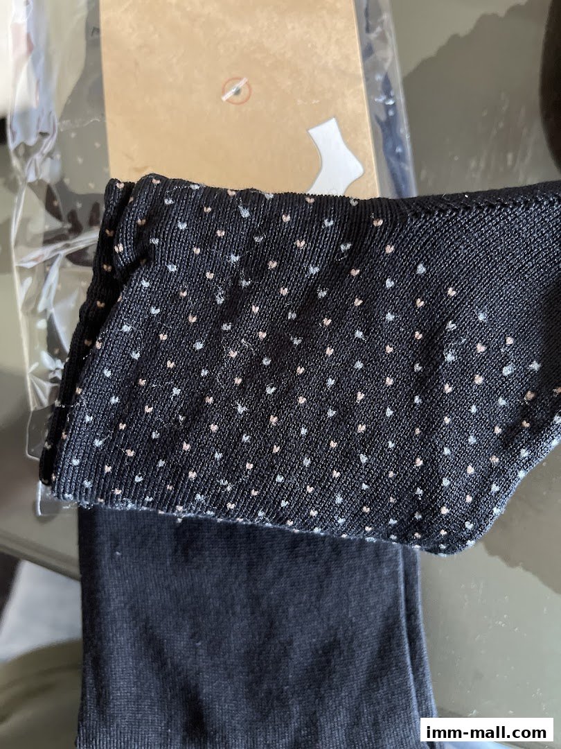 Close-up of black socks with a subtle heart pattern, packaged for sale.