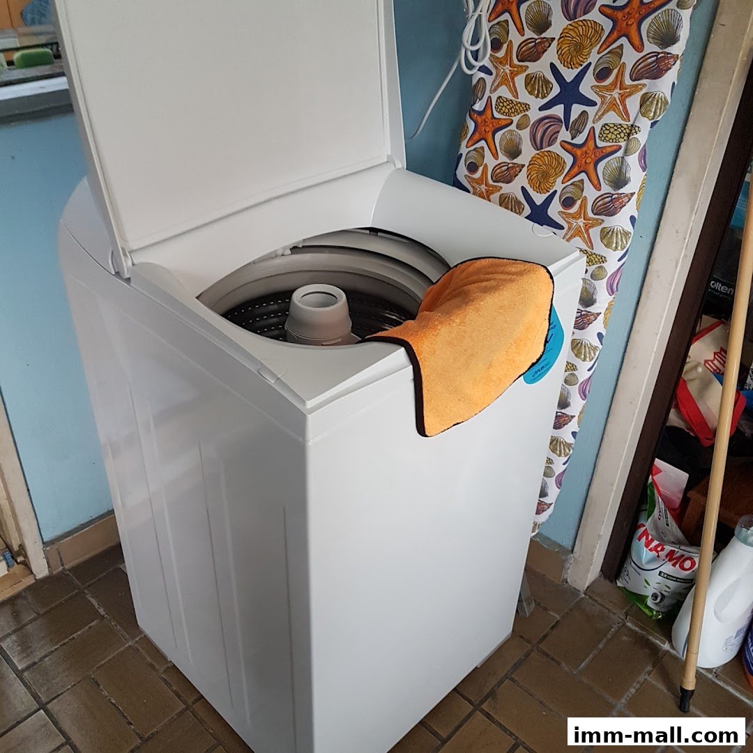 A white top-loading washing machine with an orange cloth draped over its side.