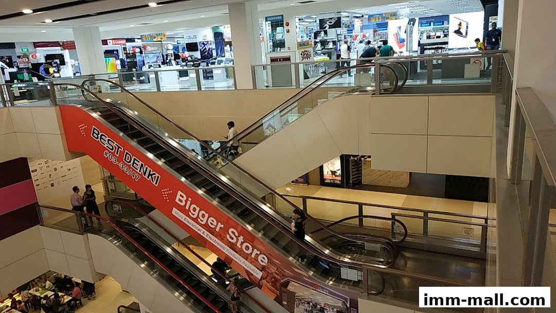 Interior view of a multi-level shopping mall with escalators and electronics stores.