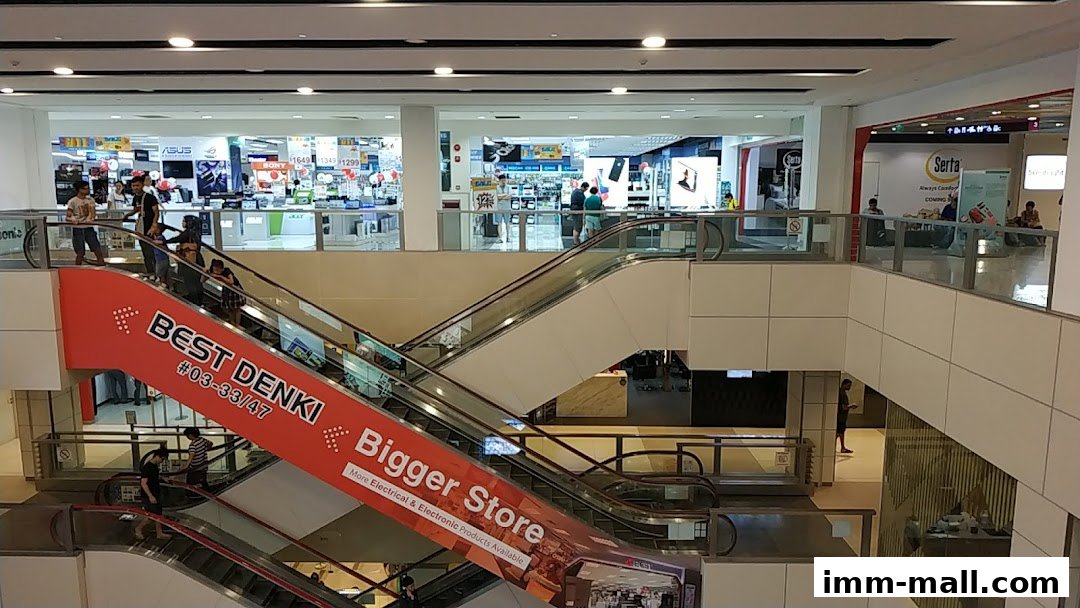 Interior view of a shopping mall with escalators and various retail stores, including Best Denki.