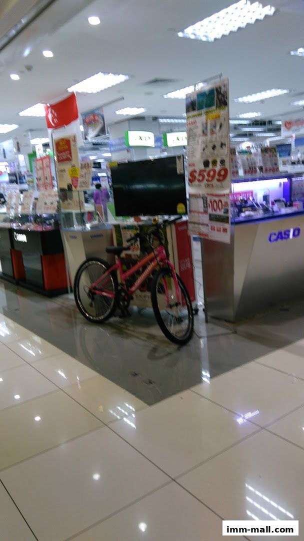 A pink bicycle is parked in front of electronics displays and a Casio counter.