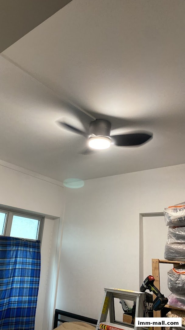 A ceiling fan with a light is illuminated in a room with a window and stored items.