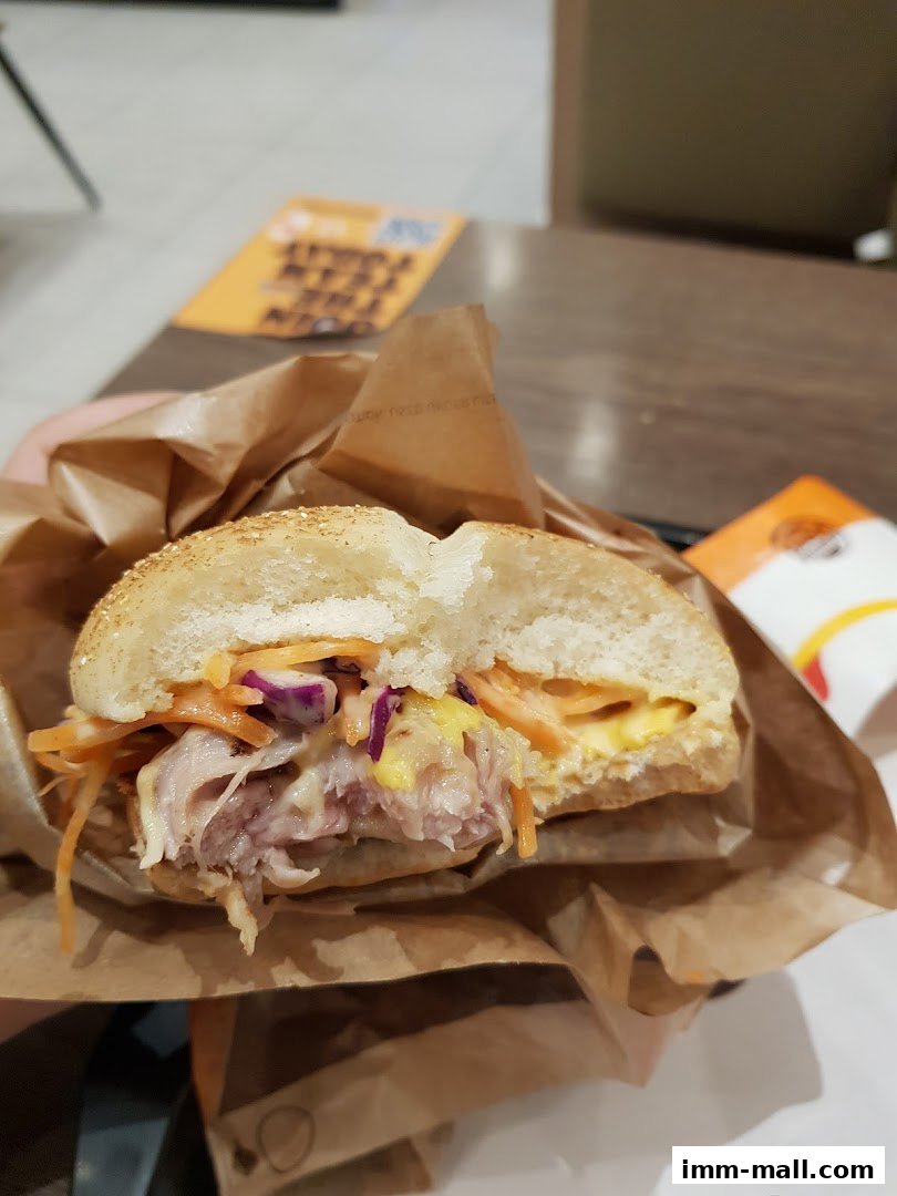 A close-up of a pulled pork sandwich with coleslaw and sauce, wrapped in paper.