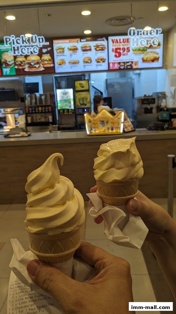 Two soft-serve ice cream cones held up in front of a Burger King counter.