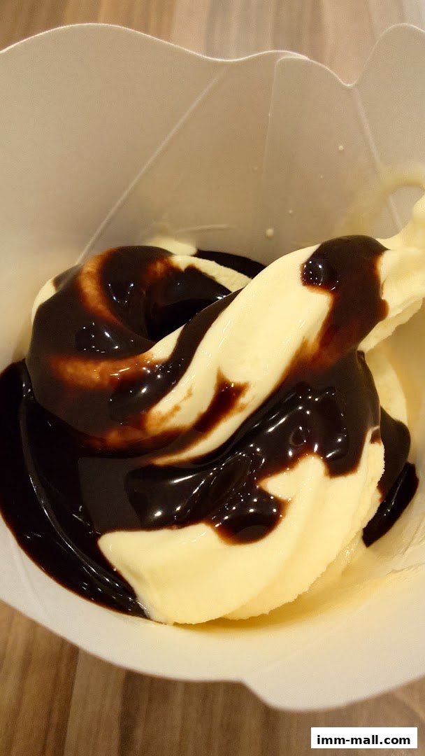 A close-up shot of a vanilla soft serve ice cream drizzled with chocolate sauce.
