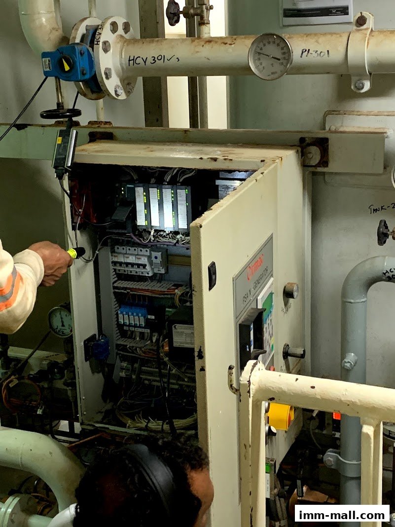 Technicians inspect an open electrical control panel with various components and wiring.