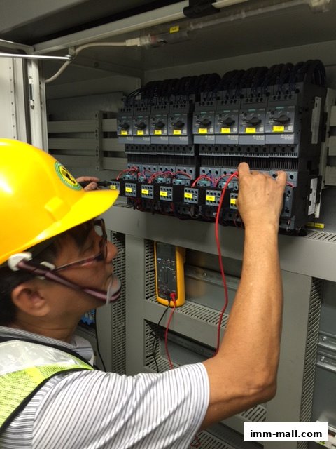 An electrician in a yellow hard hat tests electrical components in a control panel.