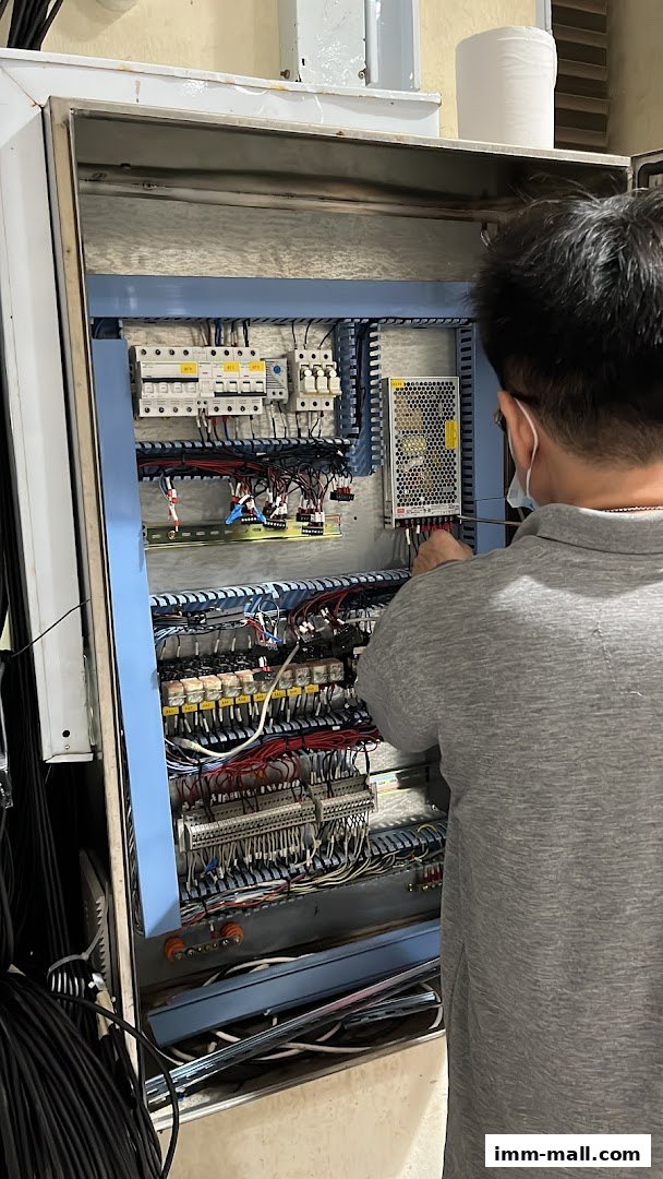 A technician works on an electrical control panel with many wires and components.