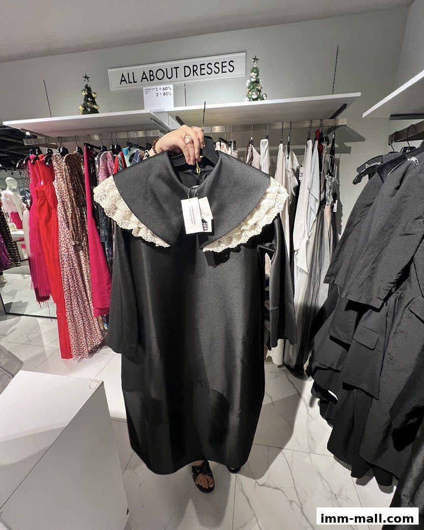 A person holds up a black dress with a lace collar in a clothing store.