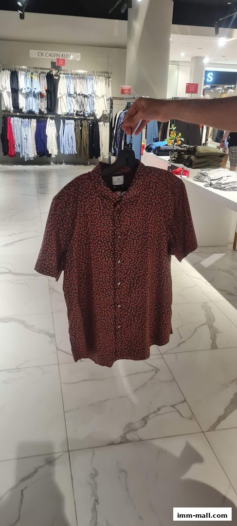 A person holds up a patterned short-sleeved shirt in a clothing store.