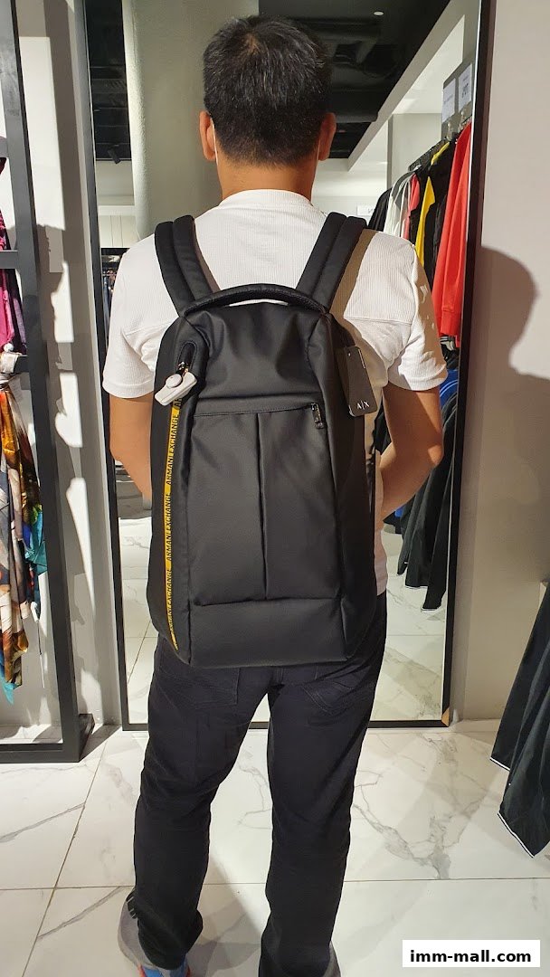 A person wearing a white shirt and black pants models a black backpack in a retail store.