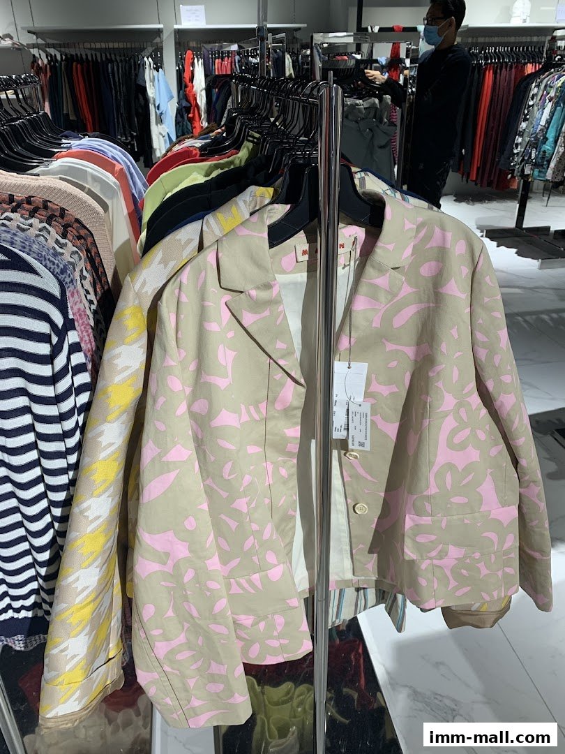A beige jacket with a pink floral pattern hangs on a rack in a clothing store.