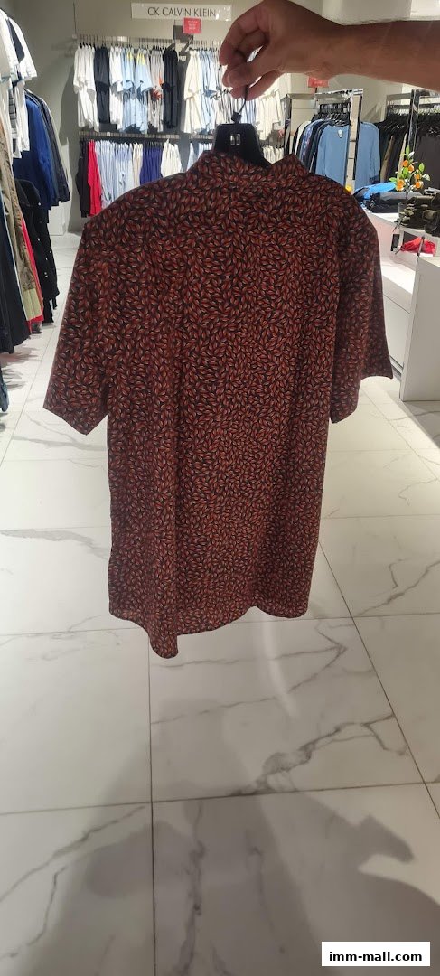 A person holds up a patterned shirt in a clothing store.
