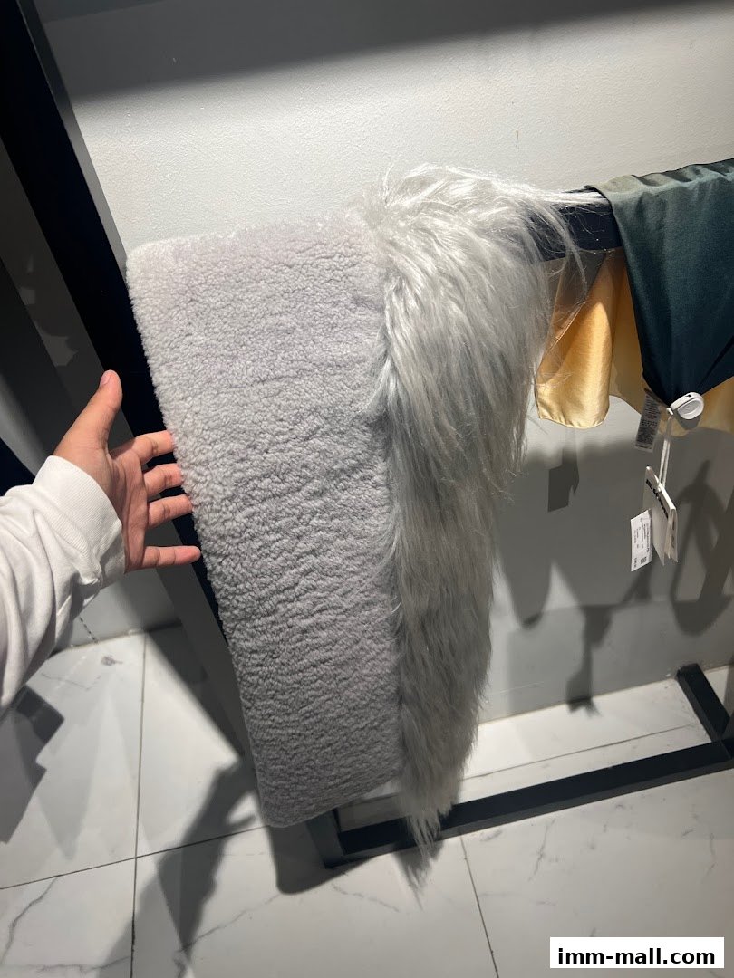 A hand touches a textured grey fabric and faux fur garment on a rack.