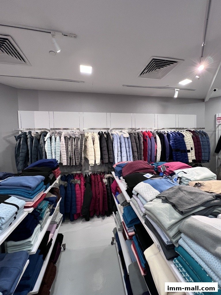Interior view of a clothing store displaying a wide selection of winter jackets and folded sweaters.