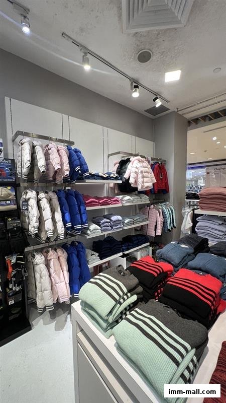Interior view of a clothing store displaying winter jackets and sweaters on shelves and racks.