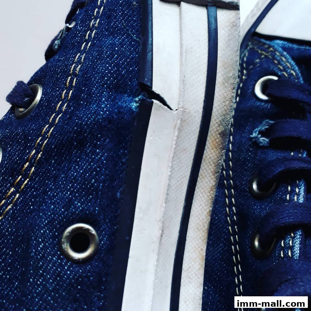 Close-up view of the iconic blue denim Converse sneakers, highlighting stitching and rubber sole details.