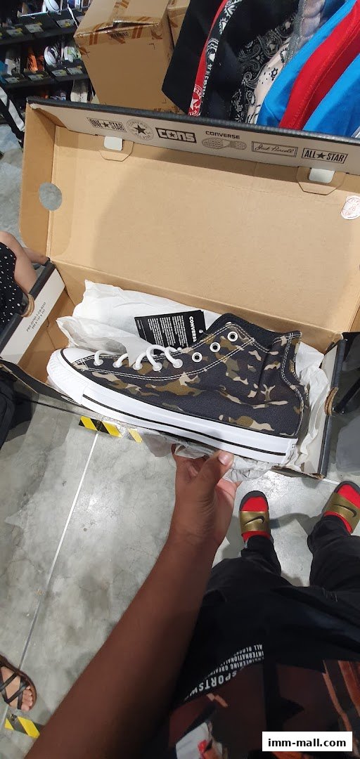 A person is holding a camouflage Converse shoe out of its box.