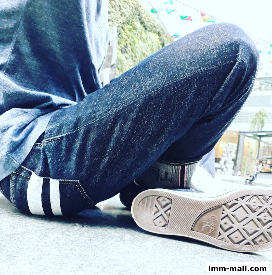 A person wearing denim jeans and Converse sneakers sits with their legs crossed.