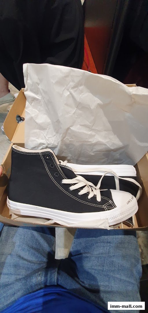 A pair of black Converse high-top sneakers in a box with white tissue paper.
