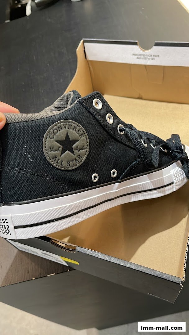A black Converse sneaker is shown inside its box, with the iconic Chuck Taylor All Star logo visible.