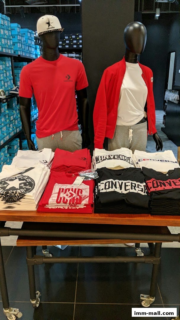Mannequins display Converse apparel, with stacks of t-shirts on a display table.