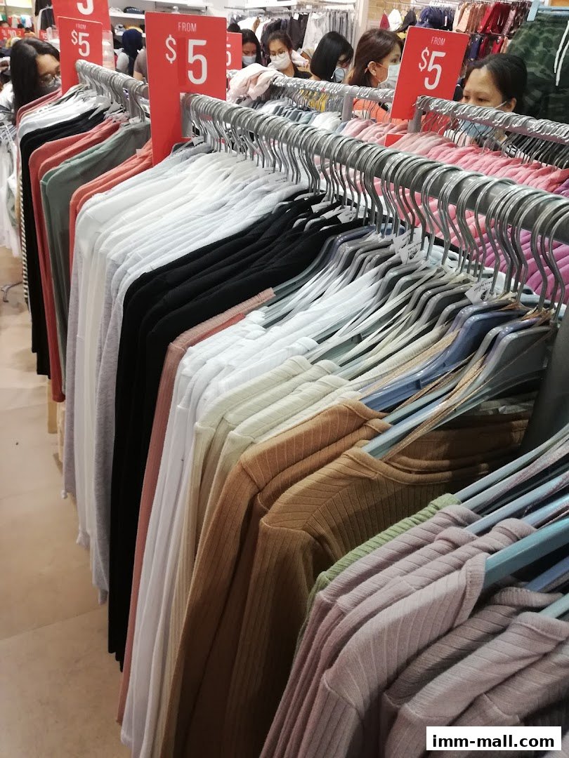 A display of various colored long-sleeved tops on hangers, with 'FROM $5' signs visible.