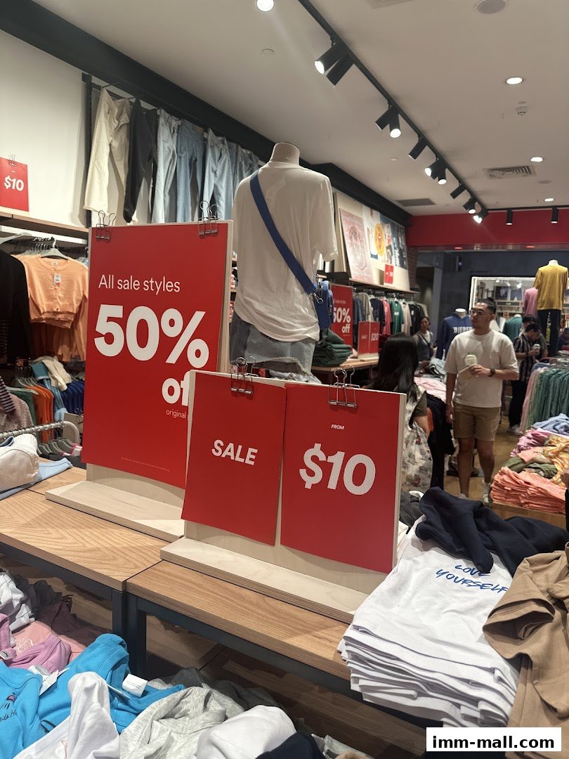A clothing store interior with sale signs, mannequins, and stacks of apparel.