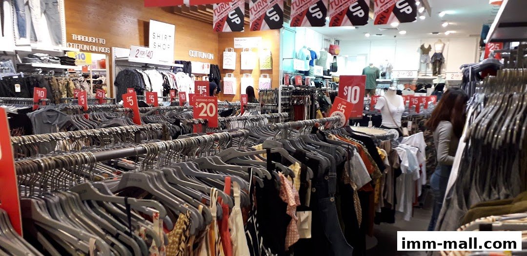 Interior view of a Cotton On store with racks of clothing and sale signs.