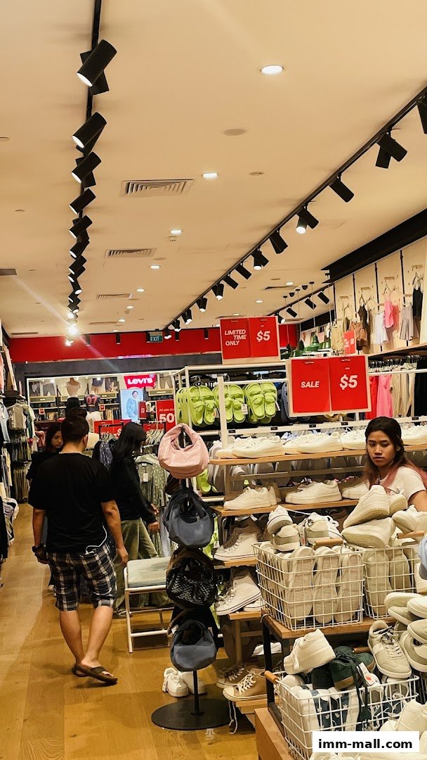 Shoppers browse footwear and apparel in a brightly lit retail store with sale signs.