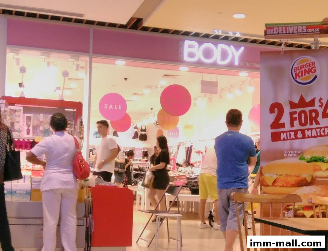 People browsing inside a Cotton On Body outlet store with sale signs and a Burger King advertisement.