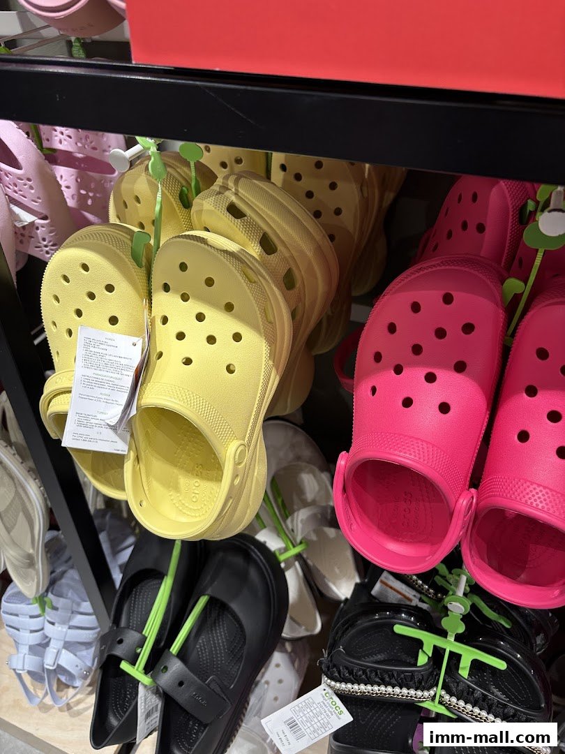 A display of colorful Crocs shoes, including yellow, pink, and black styles, on shelves.