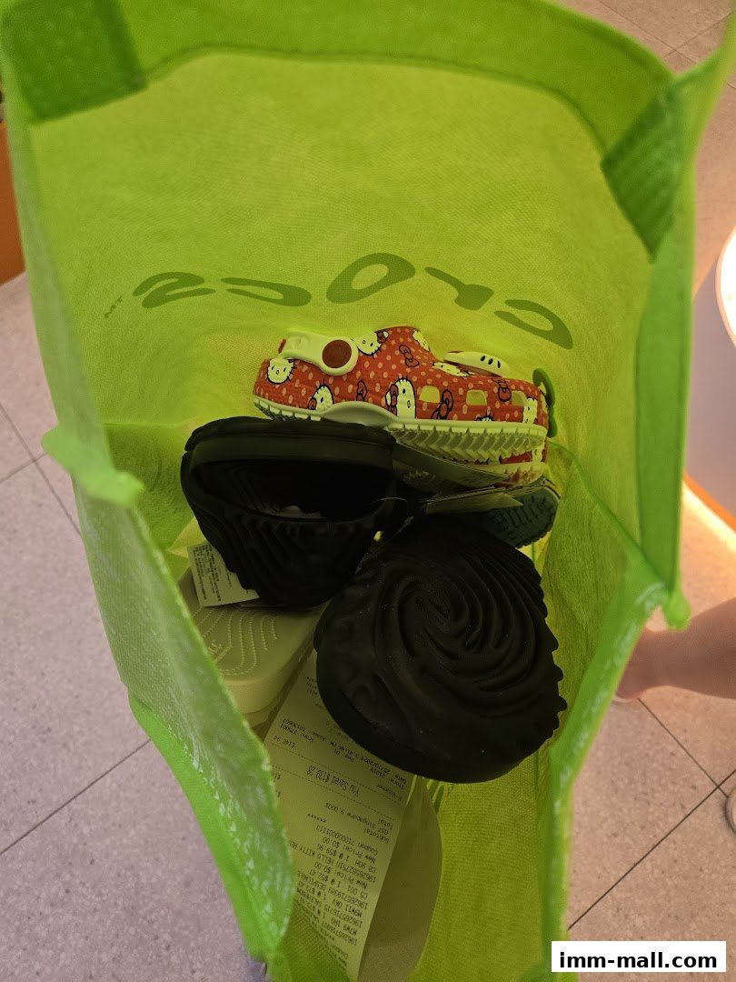 A bright green Crocs bag filled with various styles of Crocs shoes and receipts.