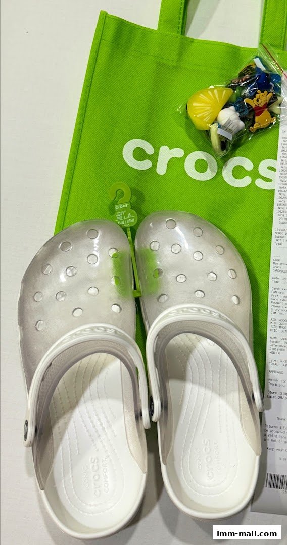 A pair of clear Crocs shoes with a green Crocs bag and Jibbitz charms.