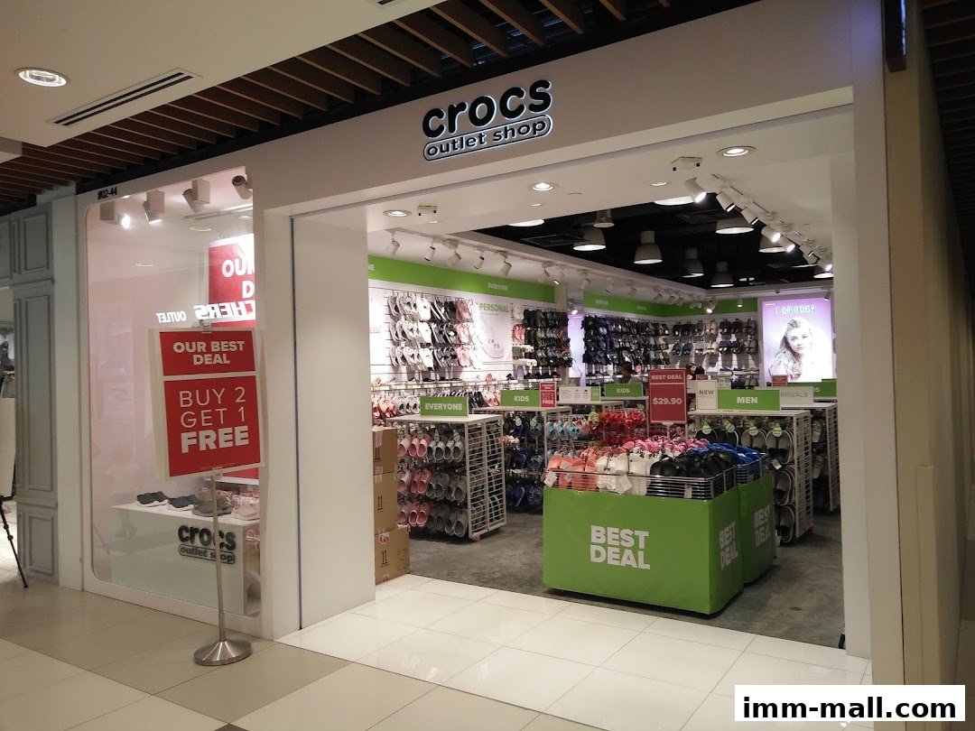 The entrance to a Crocs outlet shop displaying various footwear and promotional signs.