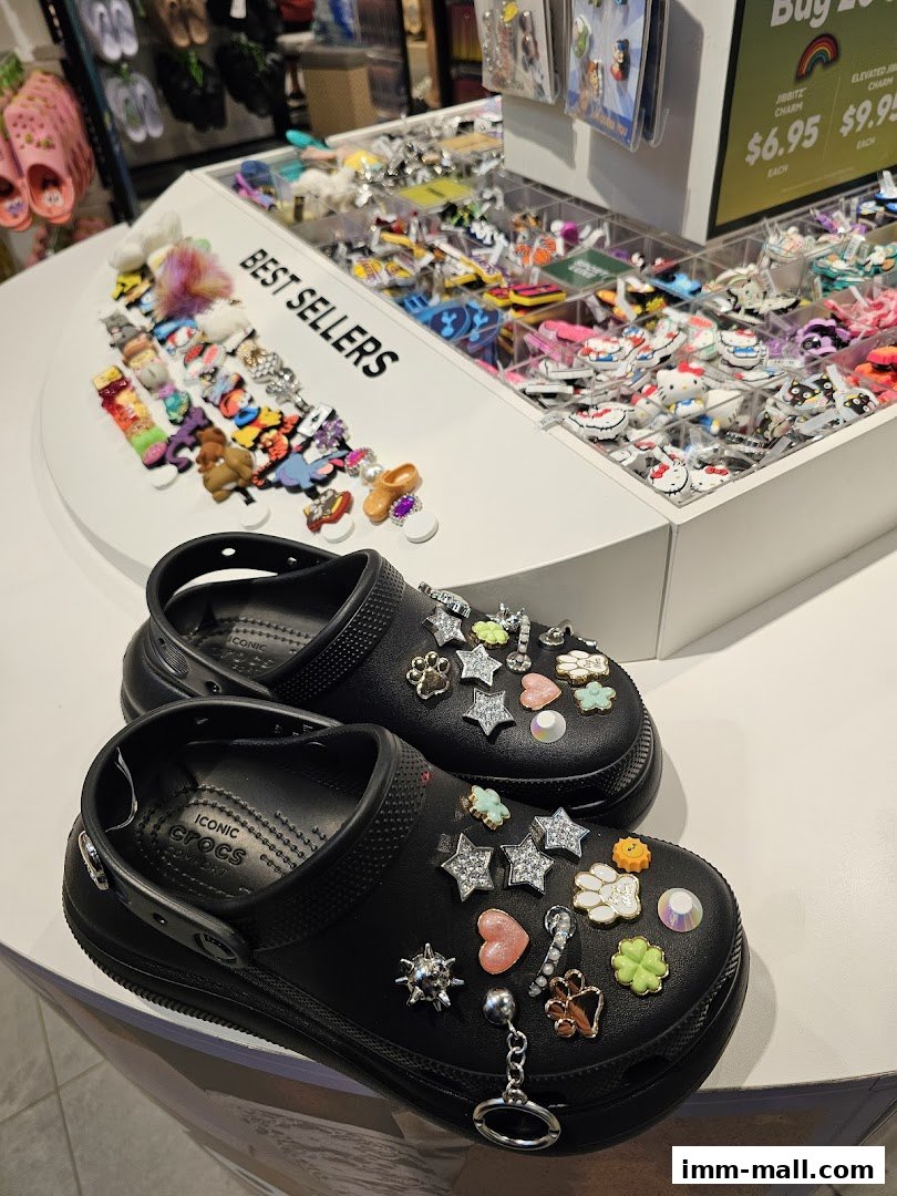 Black Crocs shoes adorned with various colorful Jibbitz charms displayed in a store.