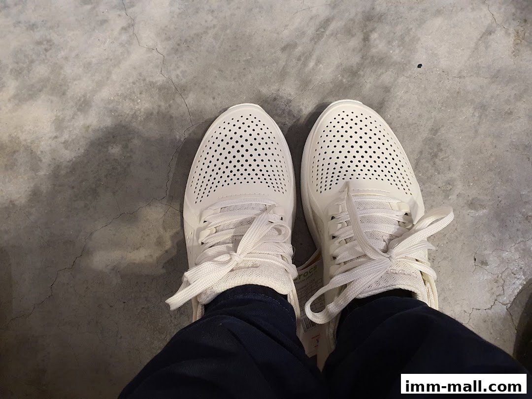 A person wearing white Crocs shoes with perforated uppers and laces.