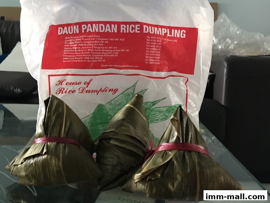 Three leaf-wrapped rice dumplings are displayed in front of a white plastic bag with shop information.