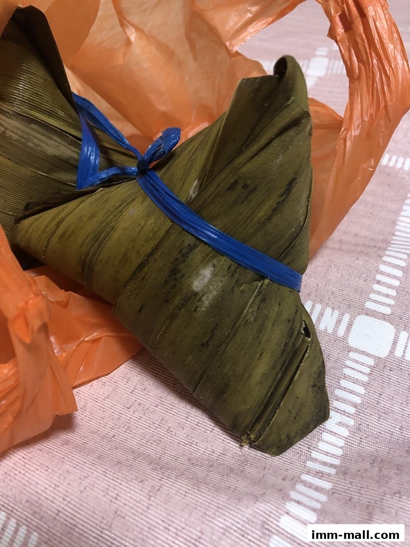 A close-up of a Daun Pandan rice dumpling wrapped in leaves and tied with blue string.