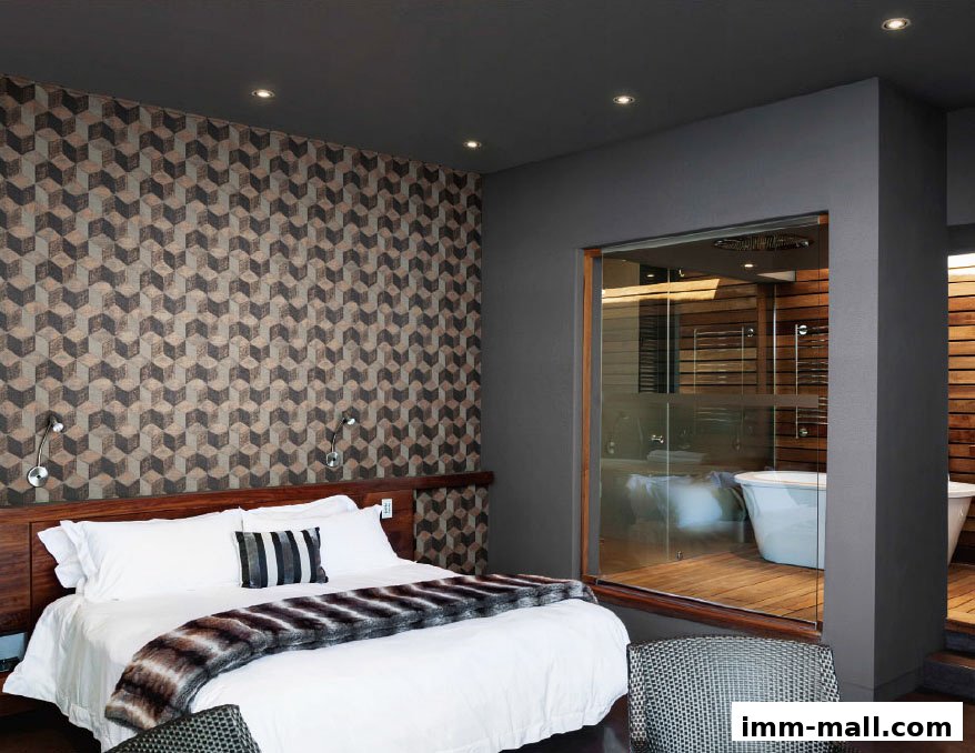 A modern bedroom with a geometric patterned wallpaper and an open-concept bathroom with a freestanding tub.