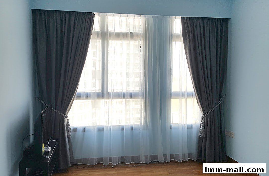 A room interior featuring dark grey curtains and sheer white curtains covering a large window.