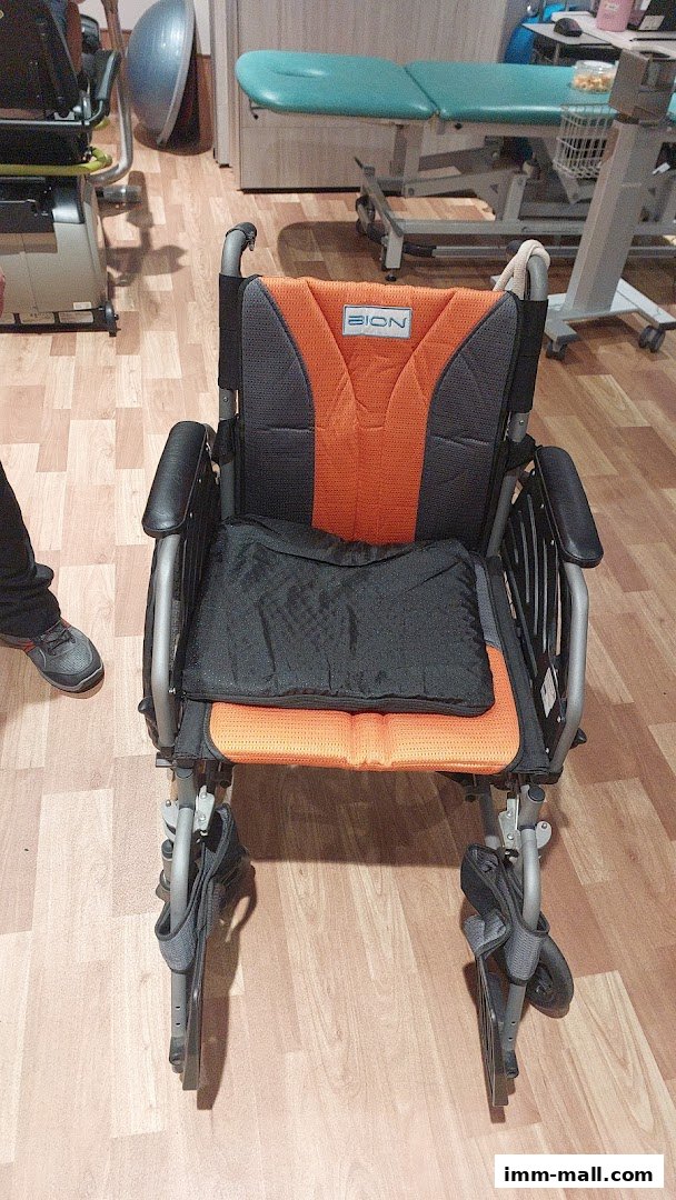 A close-up view of a modern orange and black wheelchair with a padded seat.