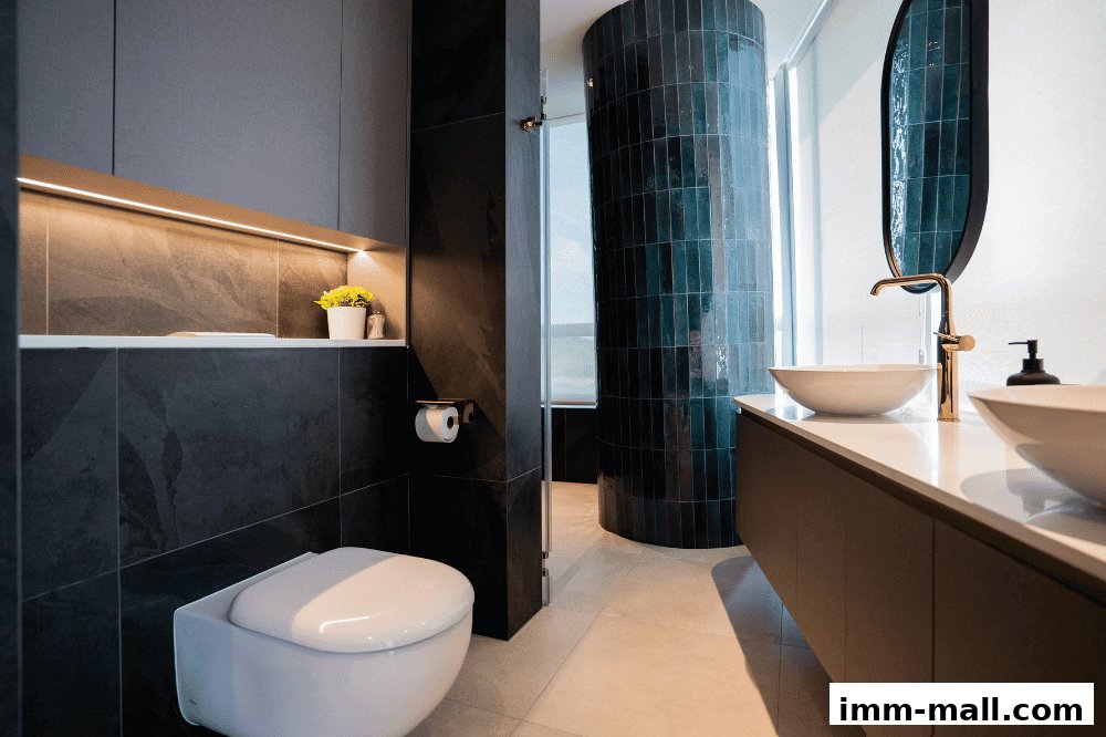 A modern bathroom with dark tiles, a wall-mounted toilet, and a vanity with two sinks.