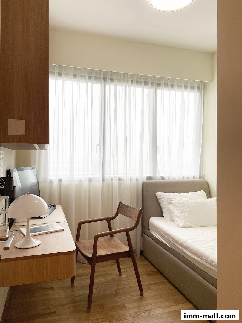 A minimalist bedroom with a desk, chair, and bed near a window with sheer curtains.